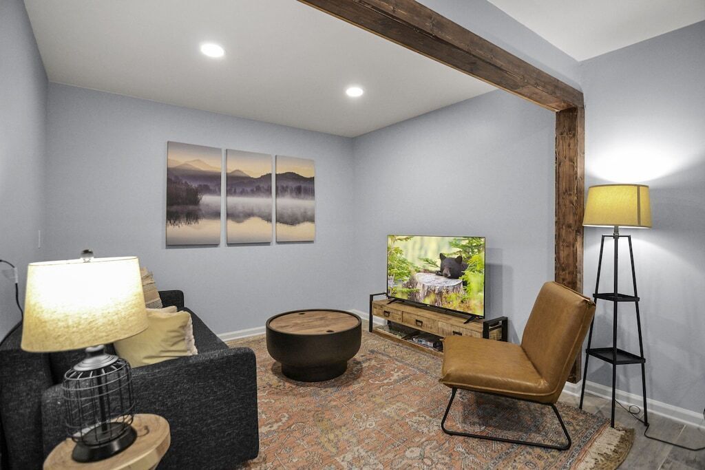 A living room with a grey couch, a round coffee table, a TV on a wooden stand, and a lamp.