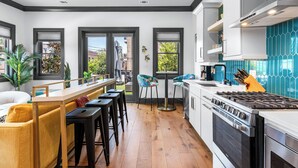 A modern kitchen with a central island, bar stools, a gas stove, and a view of the outside. - Modern Luxury Living in Unbeatable Location w/ Rooftop Deck by Lucky Savannah (Savannah)