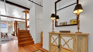 Een trap naar een tweede verdieping, een houten console tafel met lampen, en een spiegel aan de muur.