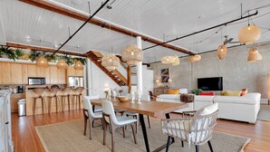 Een moderne keuken met houten kasten, een eethoek met een houten tafel en stoelen, en een zithoek met een bank en televisie.