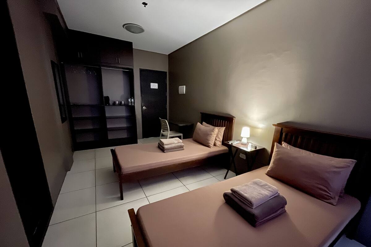 A hotel room with two single beds, a desk with a lamp, a chair, and a wardrobe.