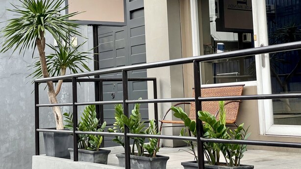 Entrada de un edificio con un letrero que dice 'INN DE AVENIDA', plantas en macetas, una barandilla metálica y una silla de mimbre.