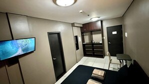 Habitación de hotel pequeña con cama, televisor, escritorio y kitchenette.