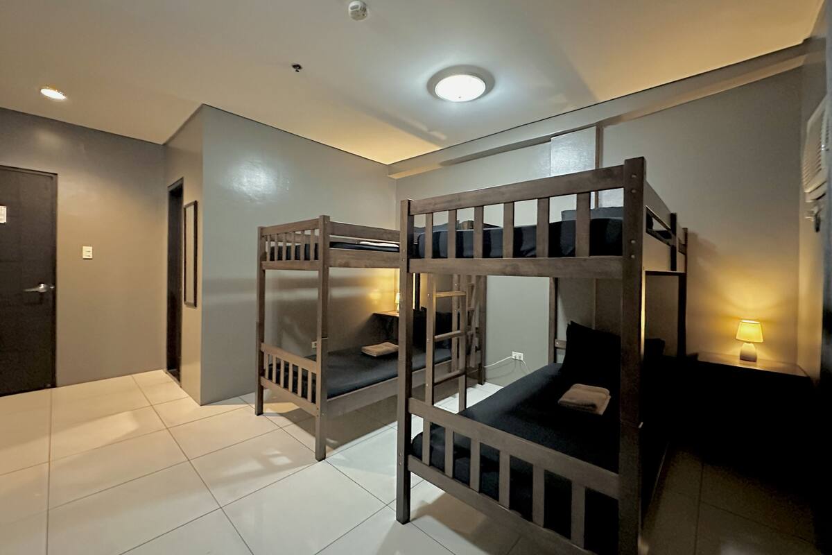 A room with bunk beds, a door, a small table with a lamp, and a ceiling light.