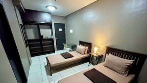 Una habitación de hotel con dos camas individuales, una mesita con una lámpara, una silla y un armario.