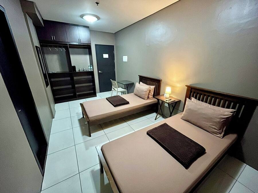 A hotel room with two single beds, a small table with a lamp, a chair, and a wardrobe.