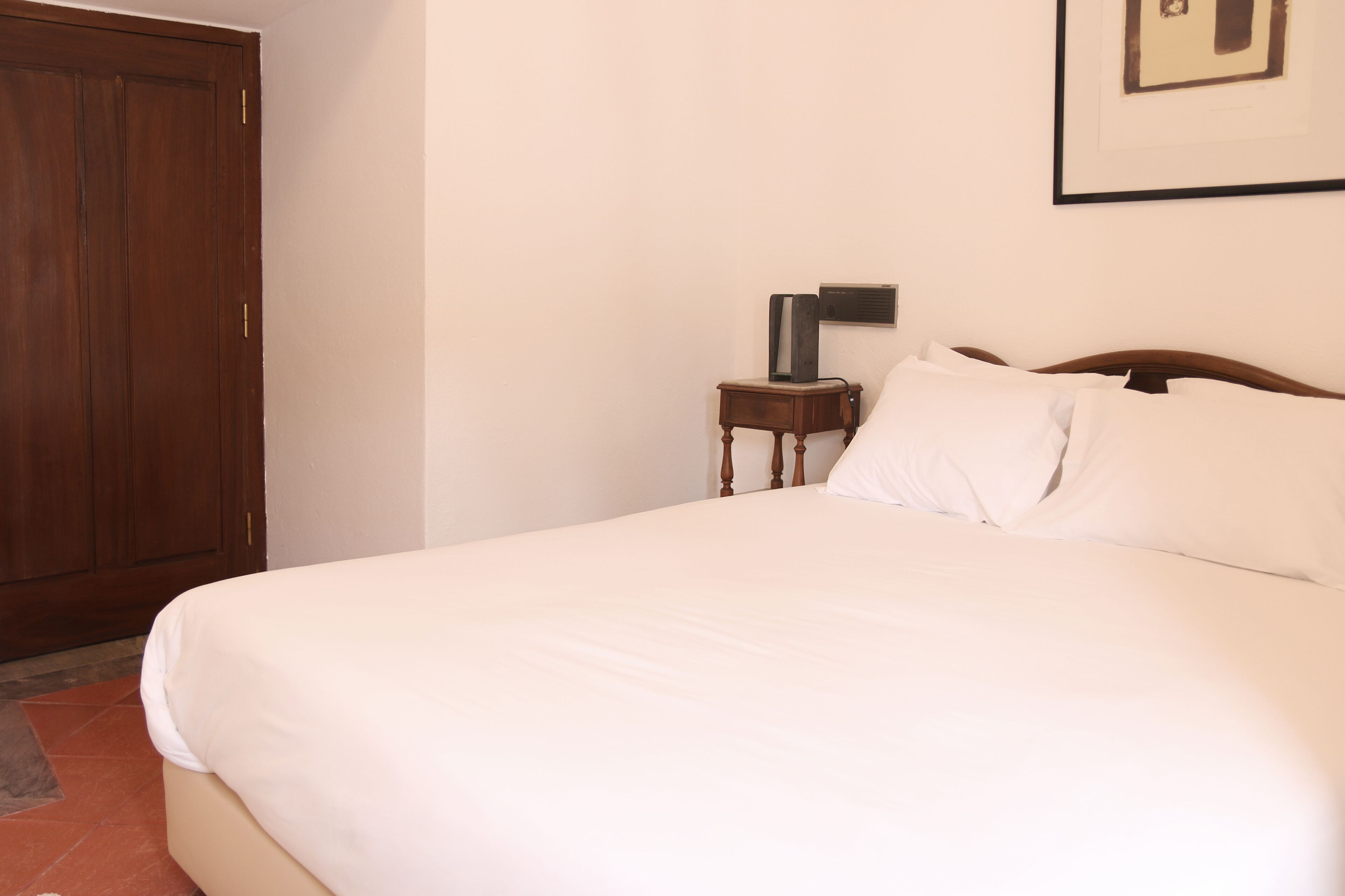 A neatly made bed with white linens, a wooden headboard, and a small bedside table with a lamp.