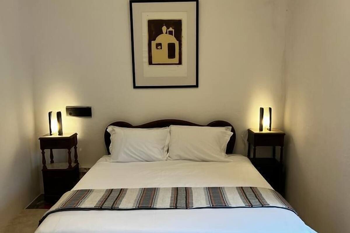 A bedroom with a large bed, two bedside tables with lamps, a framed picture on the wall, and a carpeted floor.