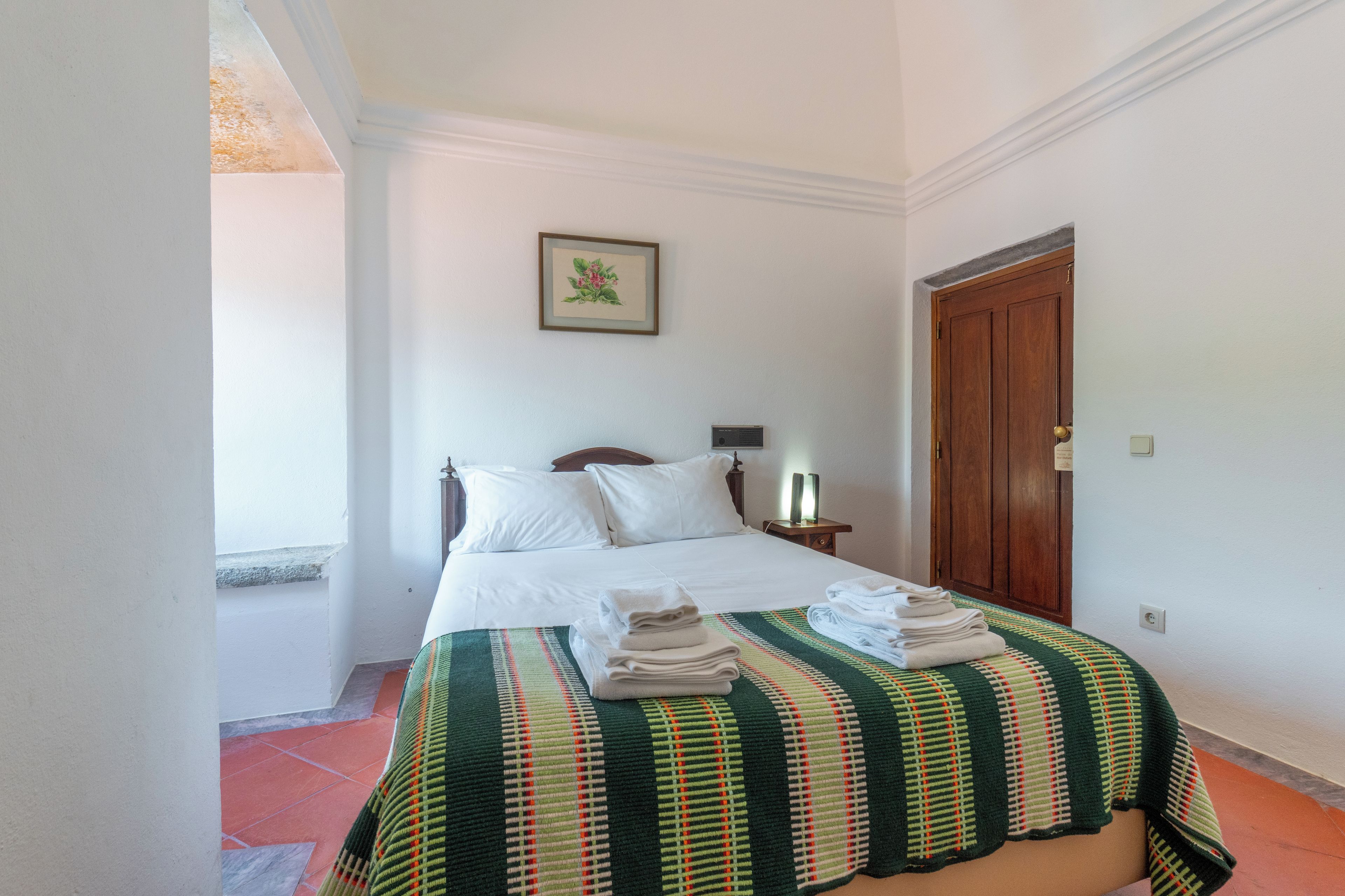 A hotel room with a bed, a nightstand, a framed picture on the wall, and a door.