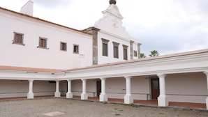 Un patio con un edificio blanco, techo de tejas y un campanario.