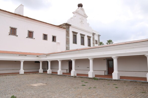 A courtyard with a white building featuring a tiled roof and a bell tower. - Convento da Orada (Reguengos de Monsaraz)