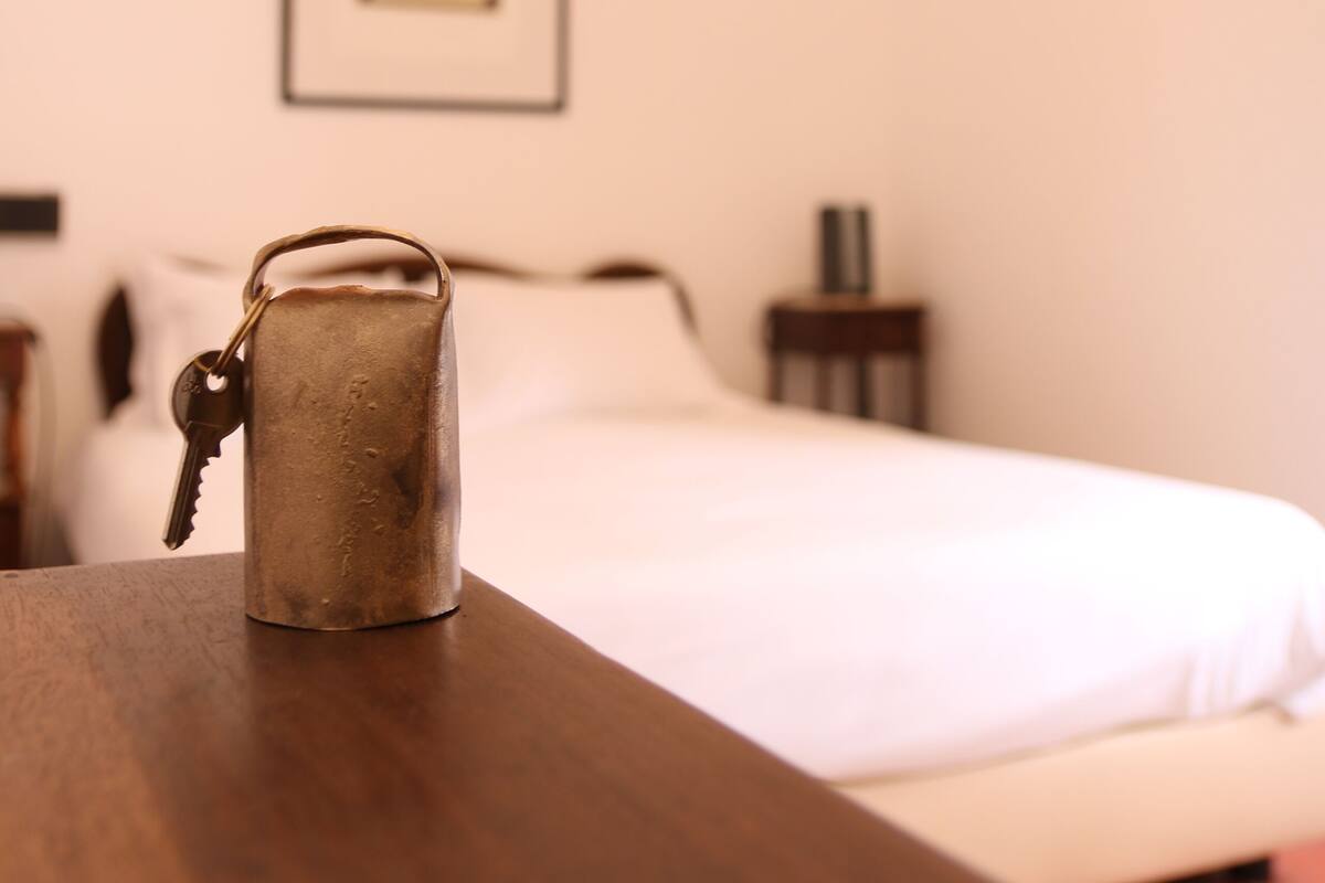 A metal mug on a wooden table in a hotel room with a bed and a framed picture on the wall.