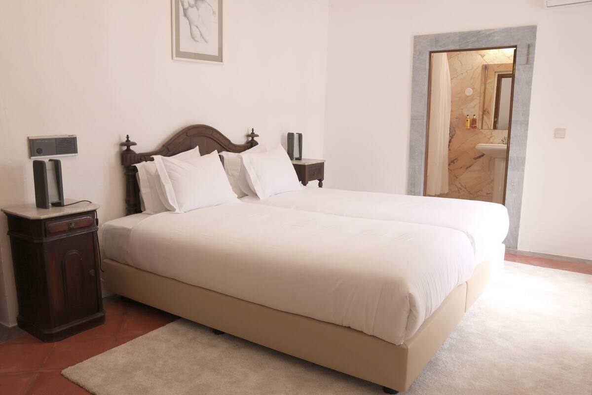 A neatly made bed with a wooden headboard, a bedside table with a lamp, and a large mirror above the door.