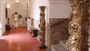 Un pasillo con piso de baldosas rojas, paredes blancas y una escalera con barandilla de piedra.