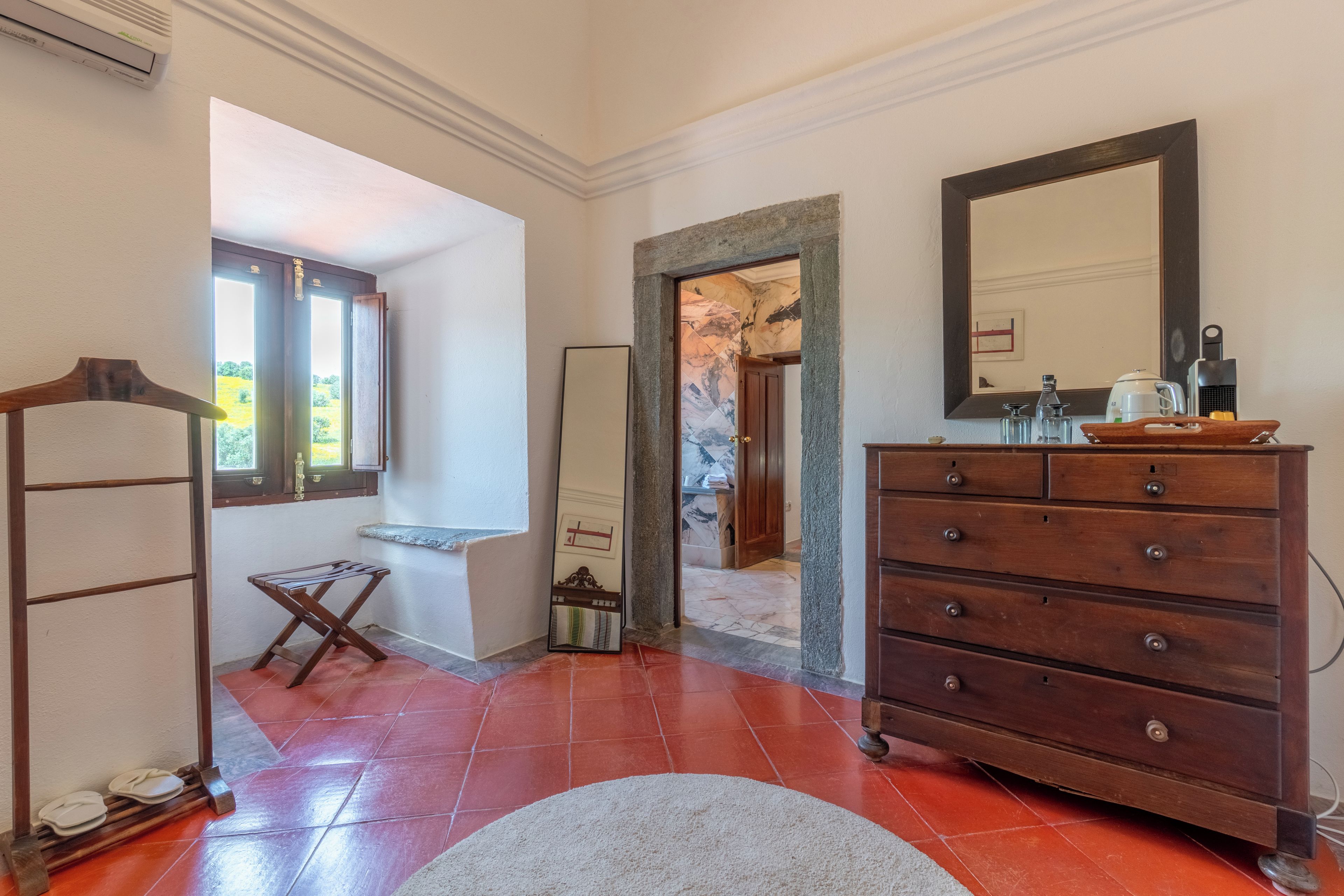 A room with a wooden dresser, a mirror, a window, and a door leading to another room.