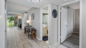 Een hal met een houten vloer, een klok aan de muur en een deur naar een badkamer.