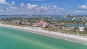Luchtbeeld van een kustgebied met een strand, een groot roze resort en een brug op de achtergrond.