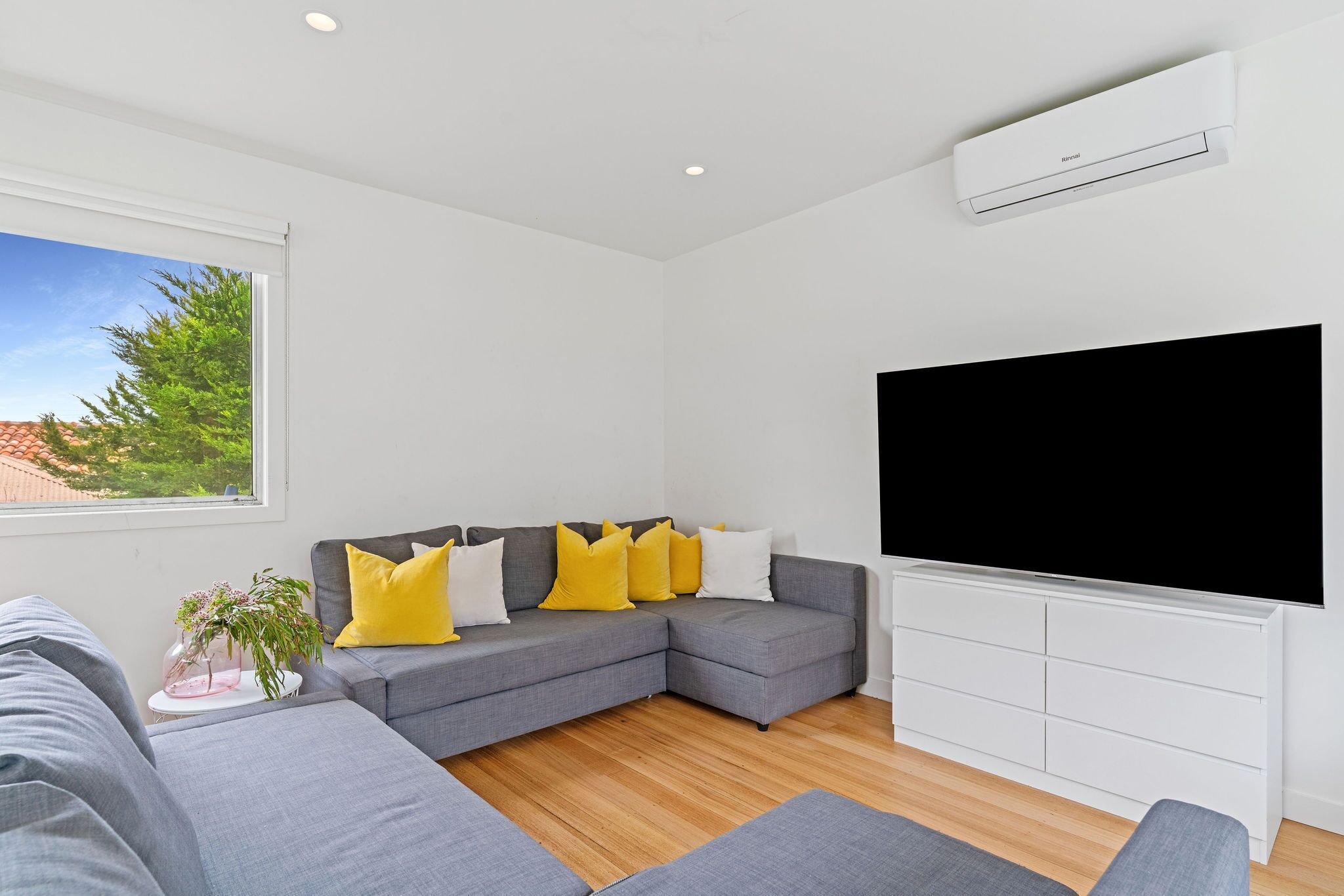 Una sala moderna con un sofá seccional gris, un televisor de pantalla plana y un mueble de entretenimiento blanco.