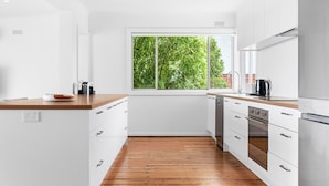 A modern kitchen with white cabinets, a wooden countertop, and a large window with a view of greenery. - Sorrento Family Fun House - Unbeatable Location (Sorrento)