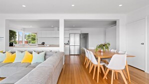 A modern living room with a grey sofa, yellow cushions, and a wooden dining table with white chairs. - Sorrento Family Fun House - Unbeatable Location (Sorrento)