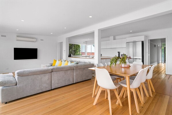 A modern kitchen with white cabinets, a wooden dining table, and a gray sofa.