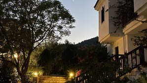 Un sendero conduce a un edificio con balcón, rodeado de árboles y arbustos.