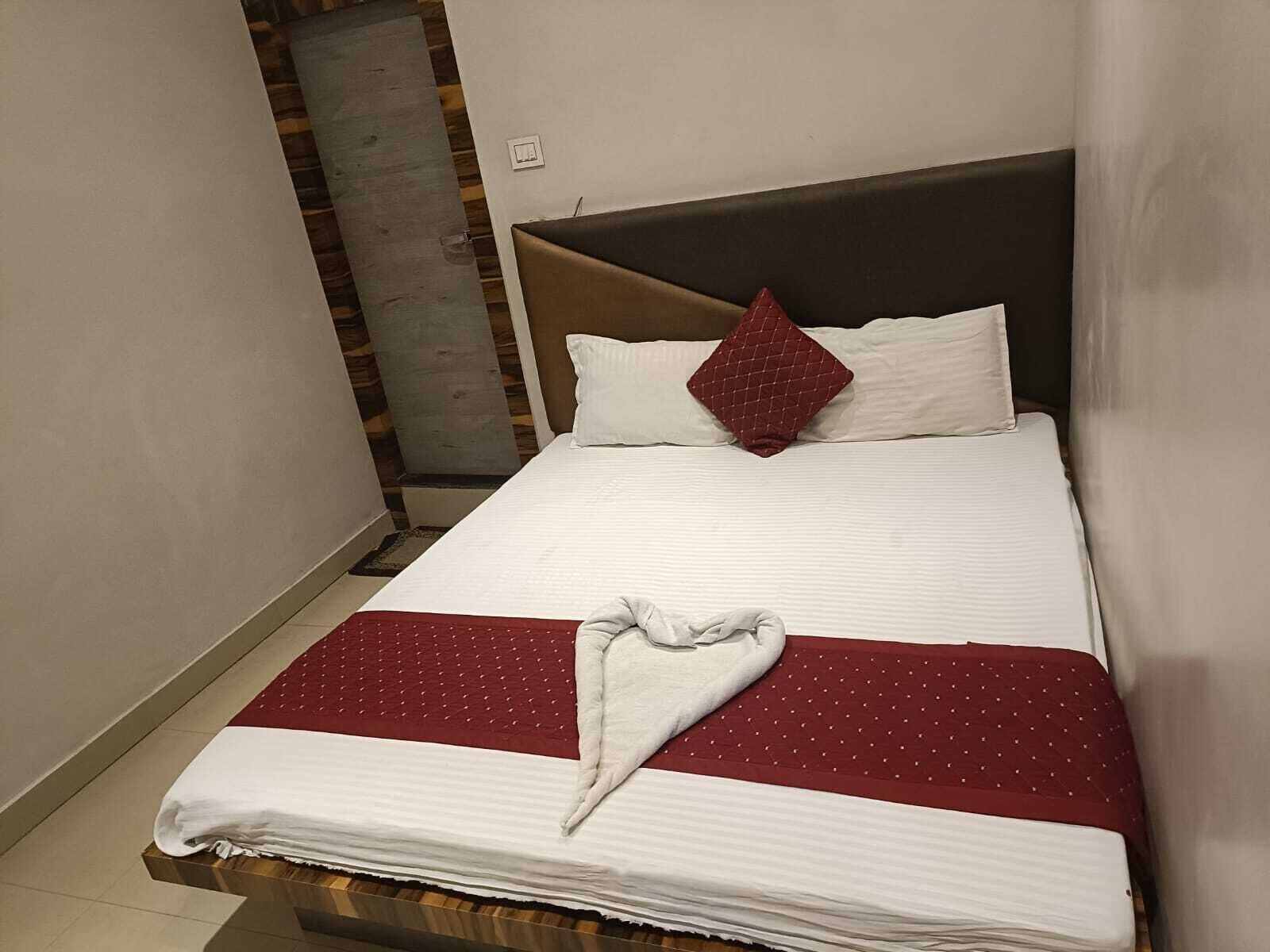 A neatly made bed with white and red bedding, a brown headboard, and a red pillow.