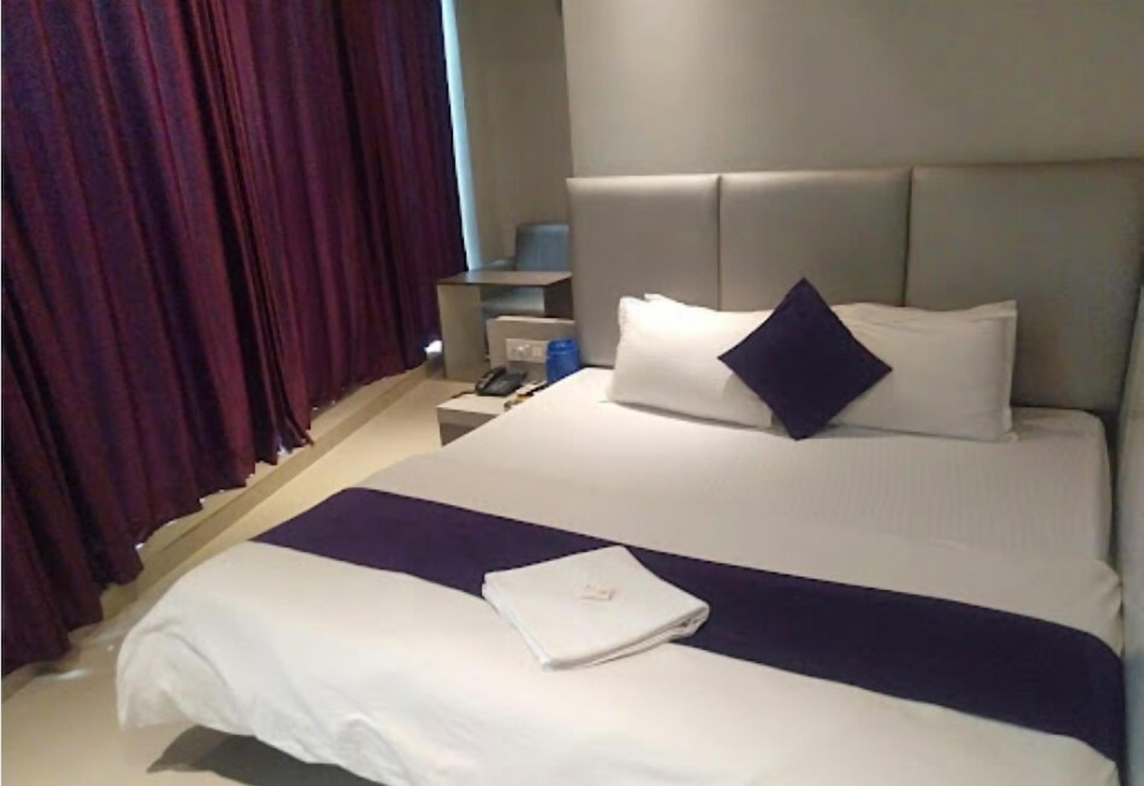 Habitación de hotel con cama, mesita de noche, teléfono y ventana con cortinas.