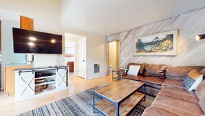 Una sala de estar moderna con piso de madera, un sofá de cuero marrón, una mesa de centro de madera y un televisor de pantalla plana montado en la pared.