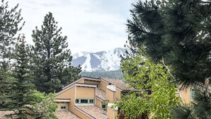 Un edificio de varios pisos con techo inclinado, rodeado de árboles y una montaña al fondo.