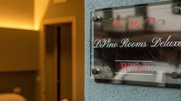 Una camera d'albergo con un letto, una insegna a parete che indica 'Divino Rooms Deluxe White' e una serratura a tastierino.