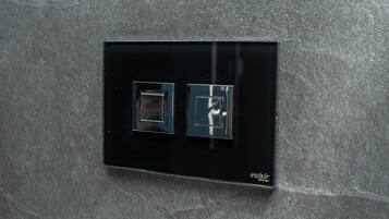 A black switch panel with two square switches on a textured wall.