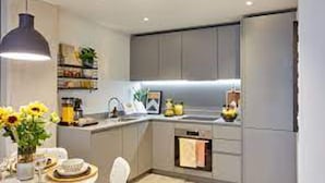 A modern kitchen with grey cabinets, a built-in oven, and a dining area with a table set for two. - Captivating 2-bed Skyview Apartment in Leeds (Leeds)