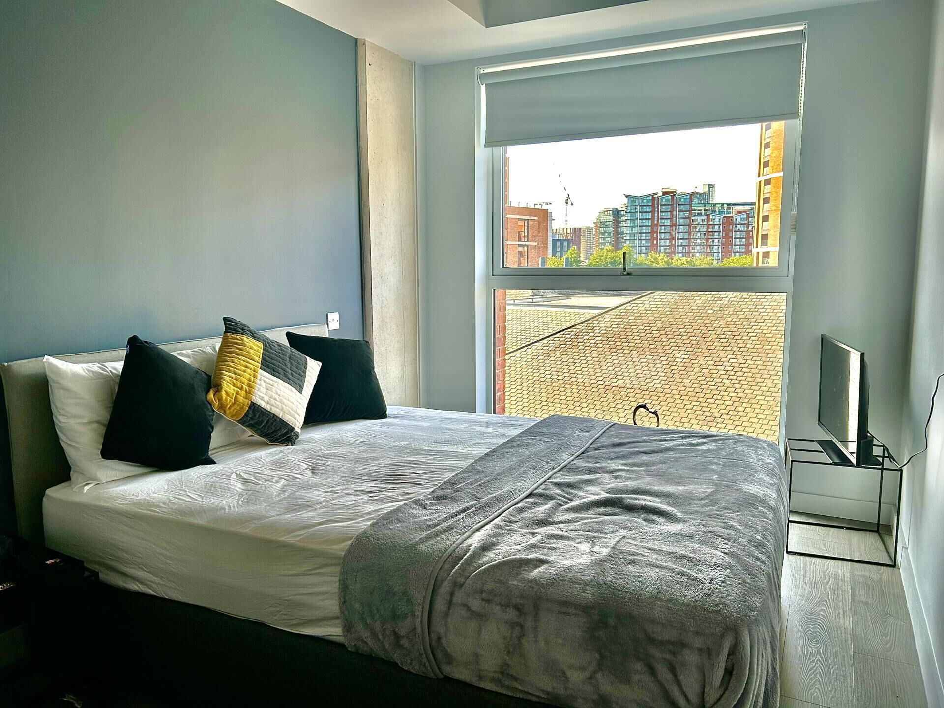 Moderni hotellihuone, jossa on suuri sänky, ikkunasta avautuva näkymä kaupunkiin ja jalustalla oleva taulutelevisio.