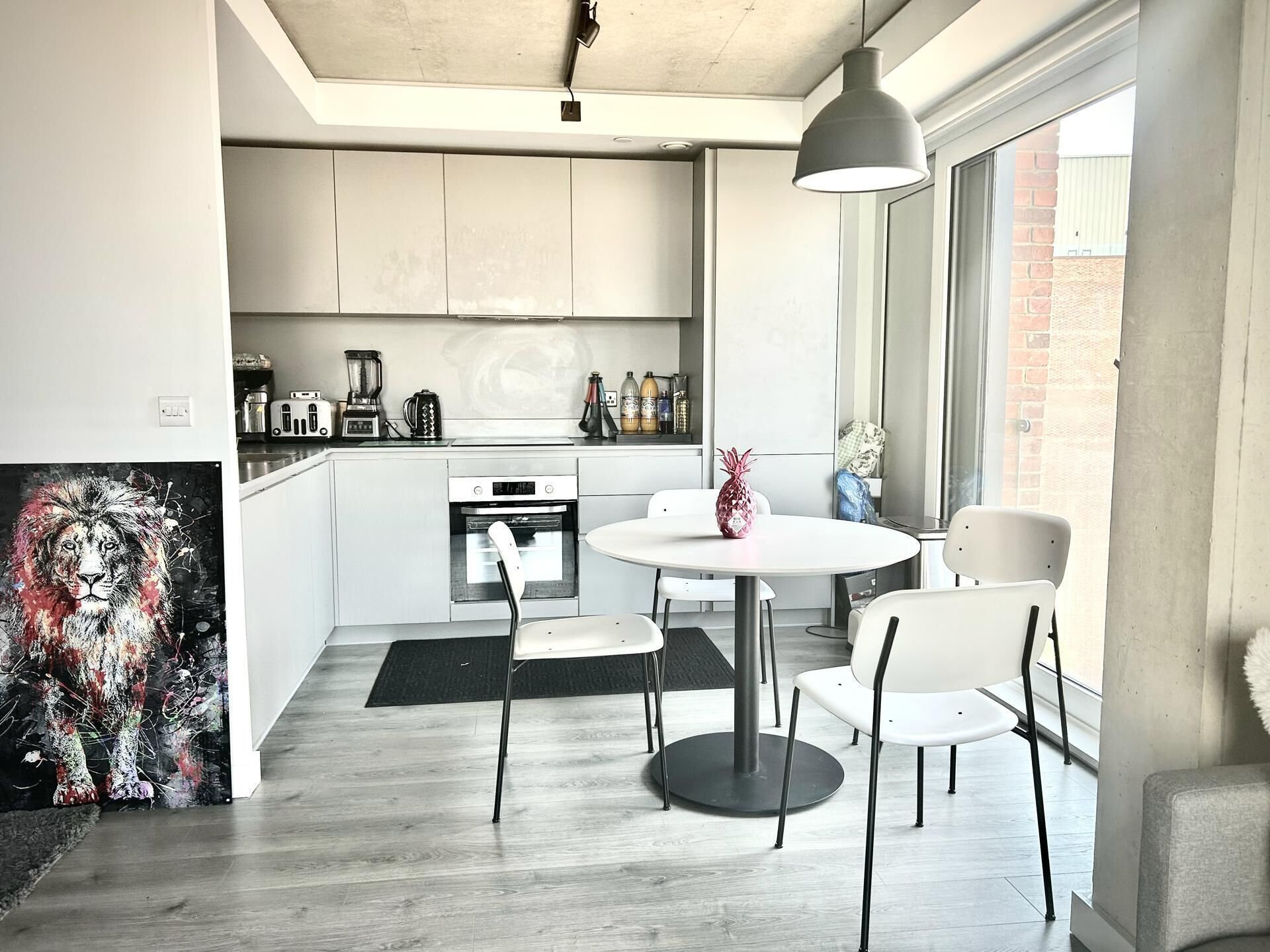A modern kitchen with white cabinets, a round dining table, and a large window.