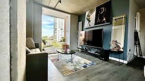 A modern living room with a large TV, a sofa, a coffee table, and a view of a cityscape through a large window. - Captivating 2-bed Skyview Apartment in Leeds (Leeds)