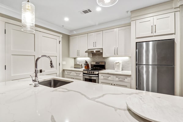 Una cocina moderna con armarios blancos, un refrigerador de acero inoxidable, horno integrado y encimera de mármol.