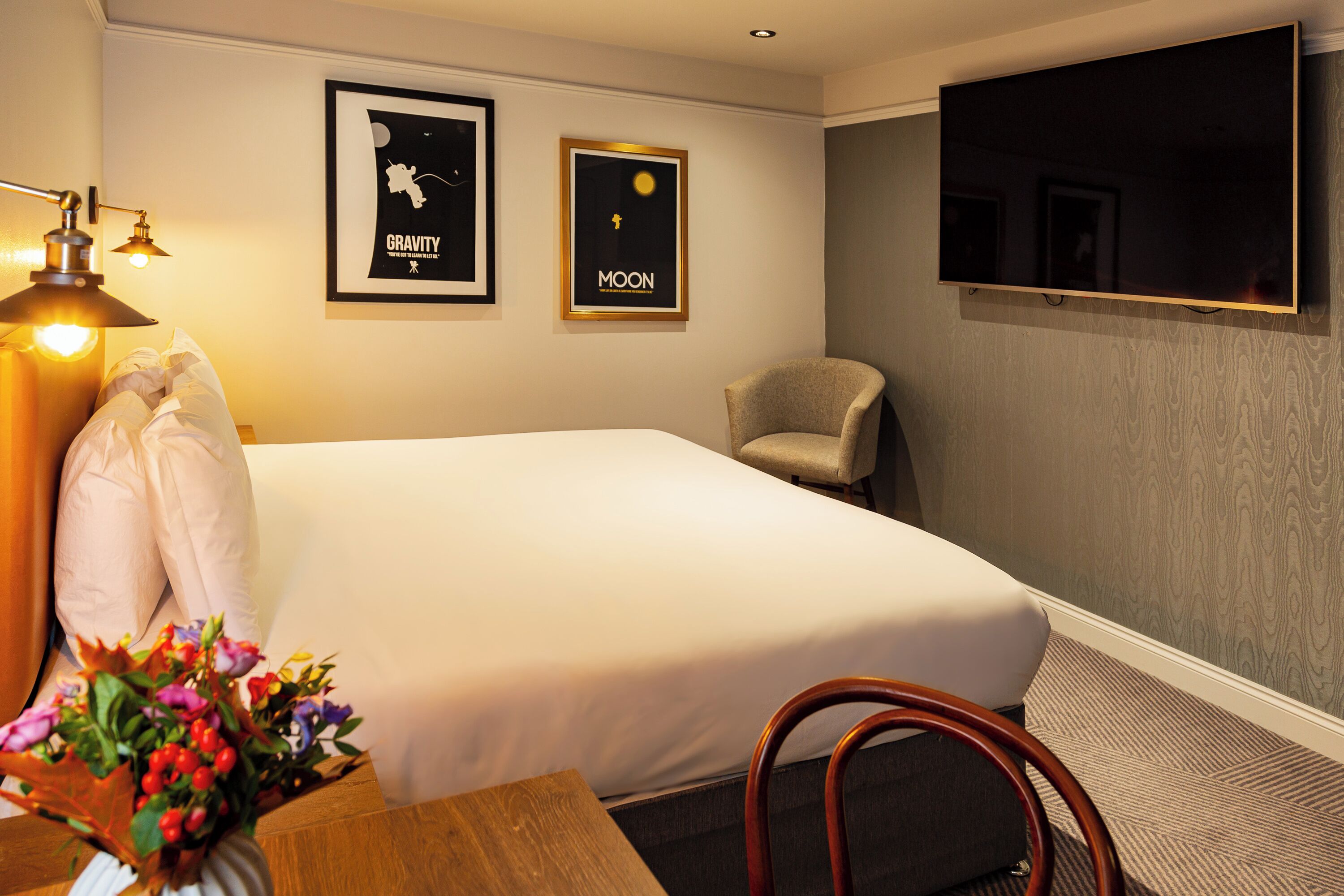 A hotel room with a bed, a chair, a desk, and a TV mounted on the wall.