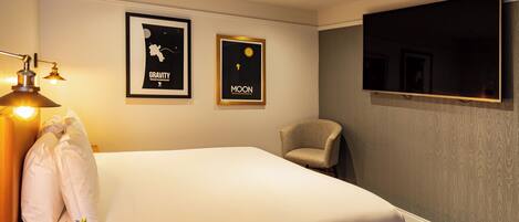 A hotel room with a bed, a chair, a desk, and a TV mounted on the wall.