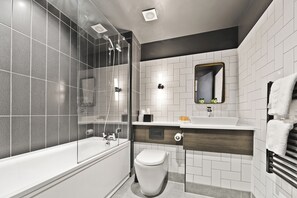 A modern bathroom with a bathtub, toilet, and glass-enclosed shower area.