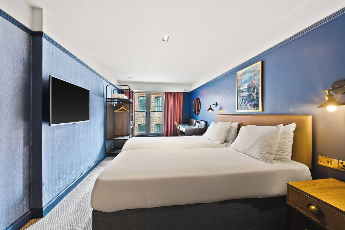 A hotel room with a large bed, a desk, a chair, and a TV on the wall.