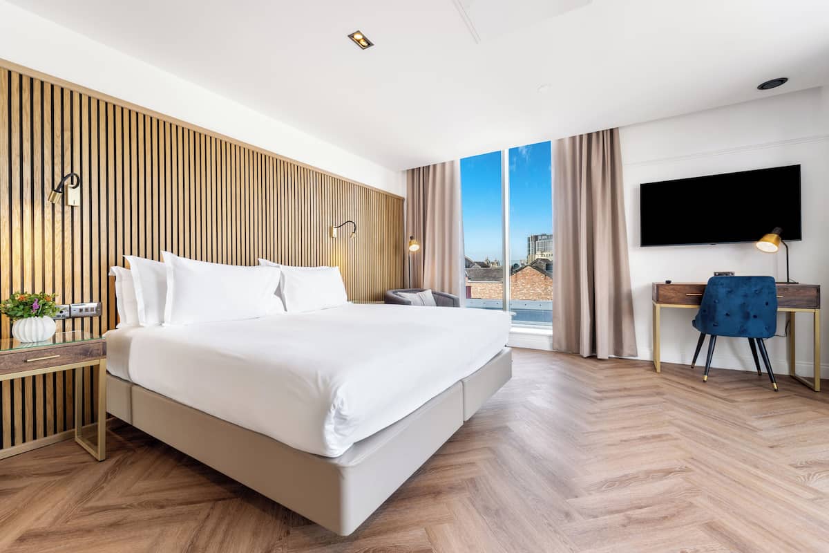 A modern hotel room with a large bed, a desk, and a TV.