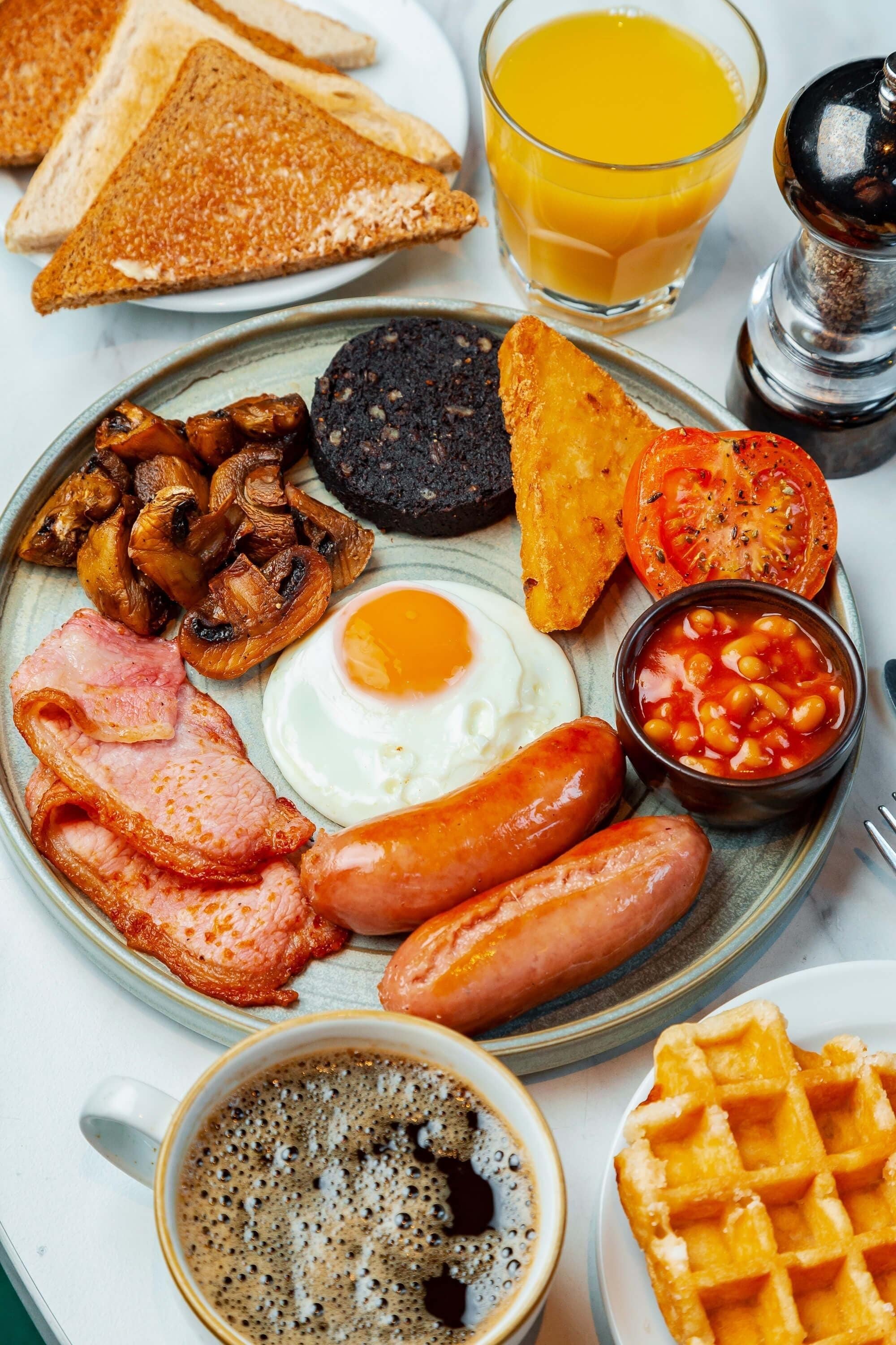 A breakfast plate with toast, sausages, eggs, mushrooms, tomatoes, beans, and a waffle.