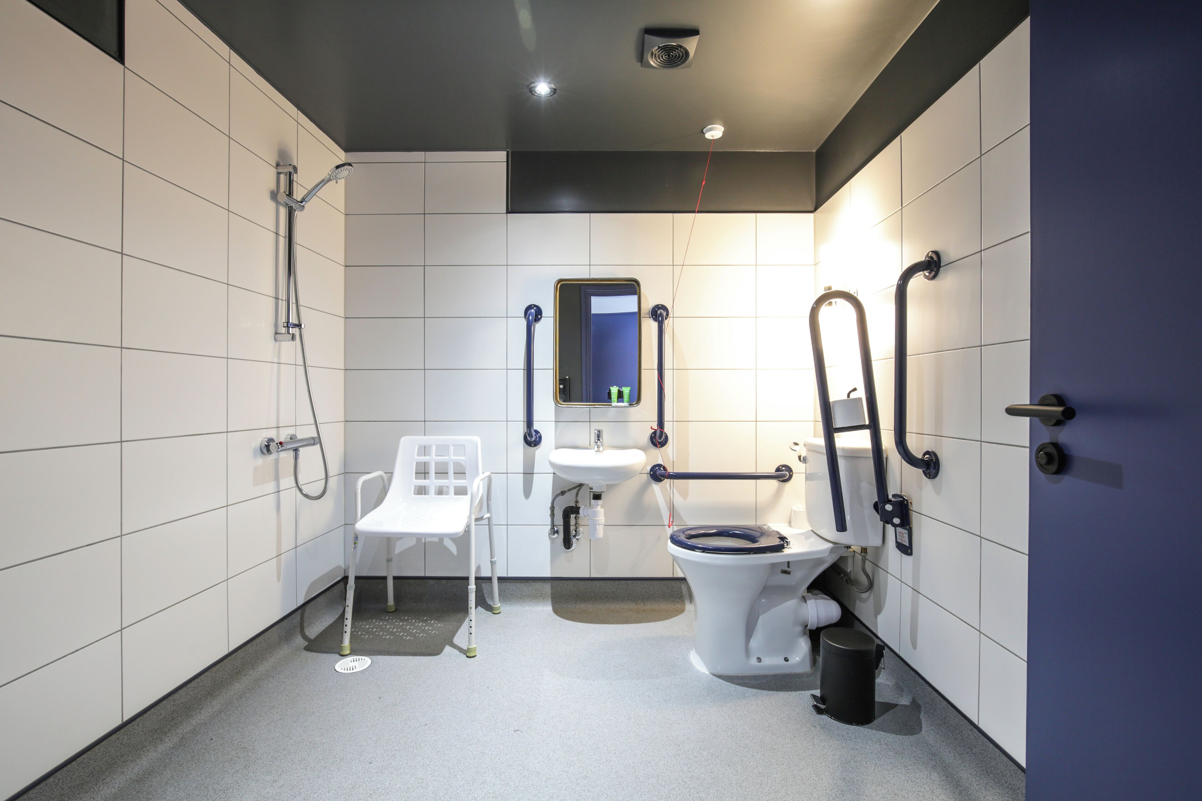 A modern bathroom with white tiles, a white toilet, a sink, a shower, and a white chair.