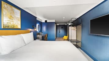 Habitación de hotel con una cama grande, un escritorio con una silla, un televisor montado en la pared y una puerta que da a un baño.