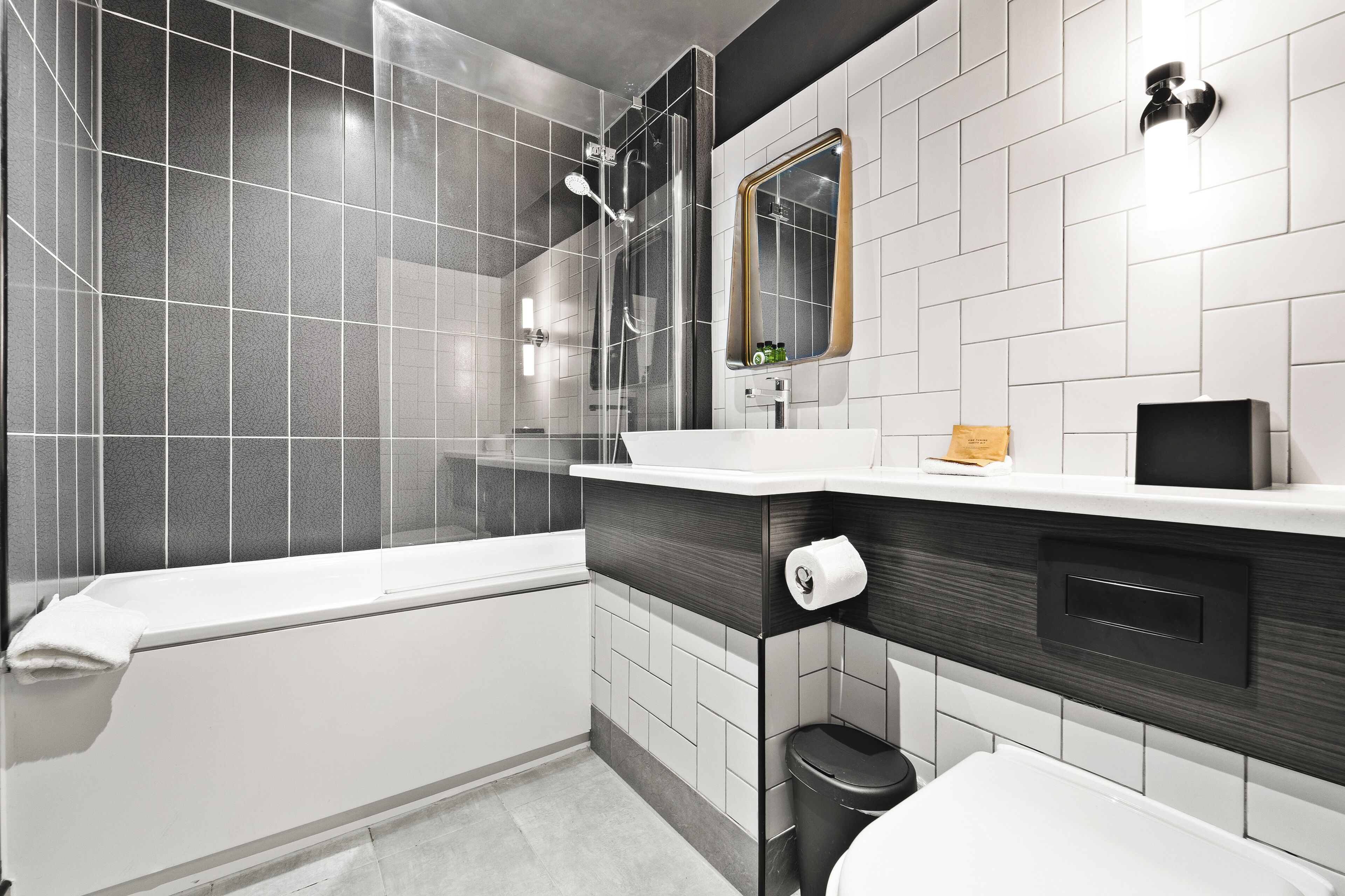 A modern bathroom with a glass-enclosed shower, a white bathtub, and a vanity with a mirror.
