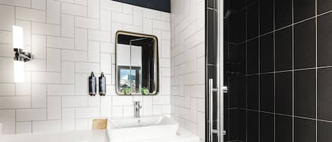 A modern bathroom with a white sink, dark wood vanity, a mirror with a gold frame, and a black tiled shower area.