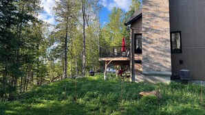 Ett modernt hus med en fasad av sten, en terrass med utemöbler och en skog som bakgrund.