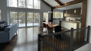 Ett rymligt vardagsrum med ett stort fönster, ett matbord i trä och ett kök med moderna vitvaror.
