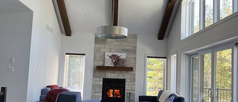 Un comedor amplio con una gran mesa y sillas de madera, una chimenea de piedra y ventanas grandes que ofrecen vistas al exterior.